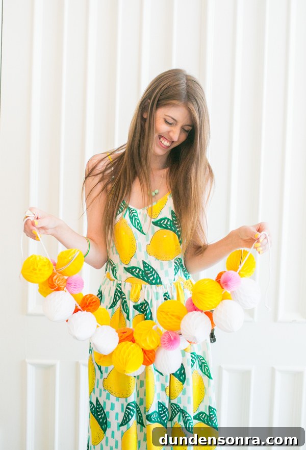 Woman in a lemon dress holding a small honeycomb garland. 