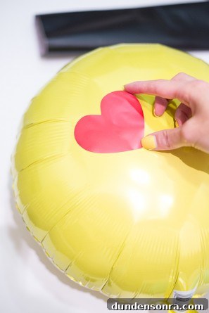 hand placing heart on emoji balloon