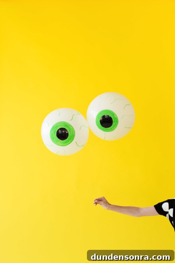 How to Make Spooky Eyeball Balloons for Halloween Decorations 5 Someone holding eyeball balloons in front of a yellow wall