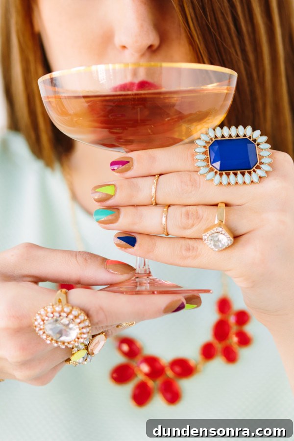 A woman with rings and colorful nails holding a drink
