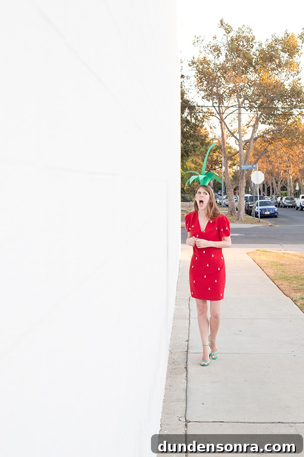 A woman in a strawberry costume walking on the side walk 