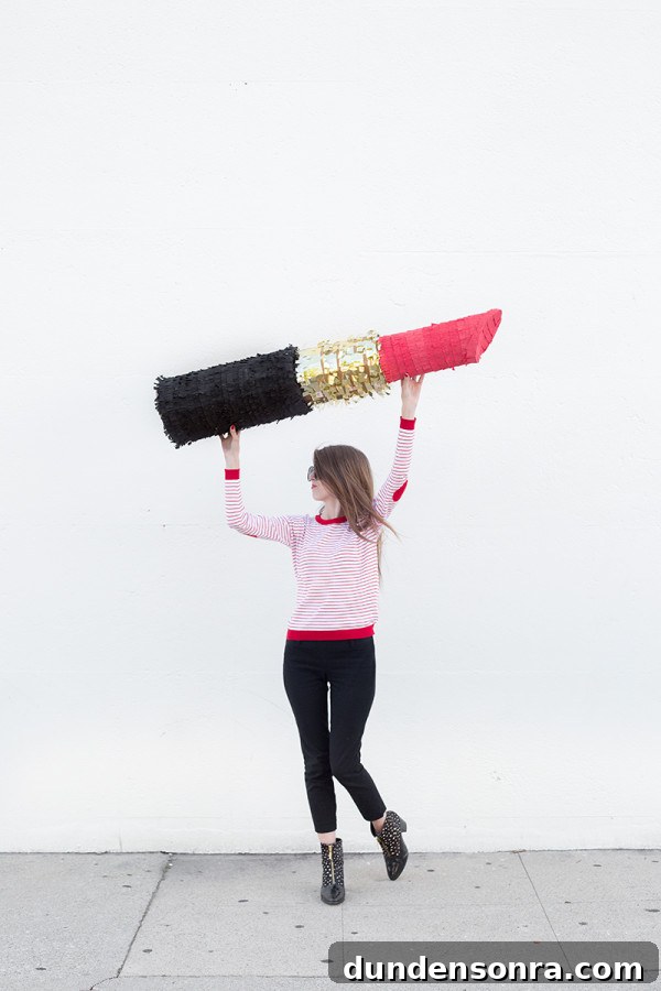 A woman holding a big lipstick piñata 