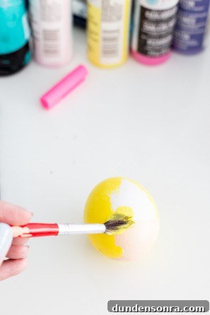 Someone painting an egg yellow