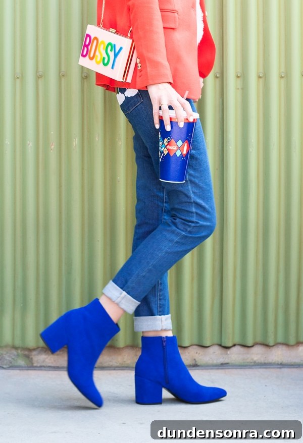 3 Bold Colorful Fall Outfits to Elevate Your Wardrobe 3 A close up of a woman in jeans and blue boots holding a drink