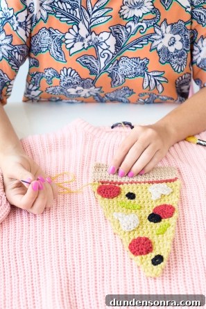 Someone sewing a slice of pizza onto a pink sweater