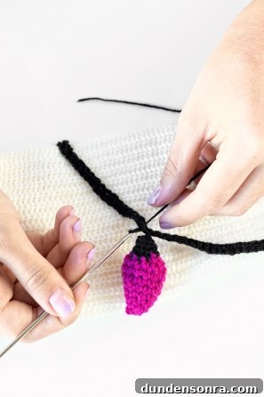 Someone sewing a pink item on a white sweater