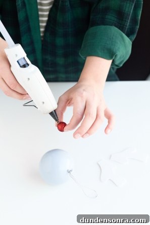 Someone gluing a red ball on a purple ornament 