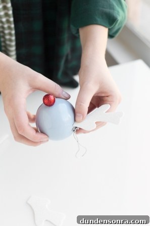 Make Rudolph Reindeer Ornaments: Step-by-Step DIY Guide 6 Someone gluing a white object on a purple ornament