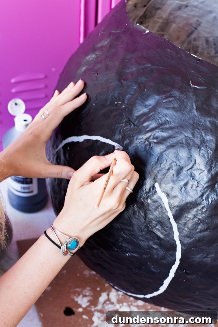 Someone painting white on a black newspaper ball
