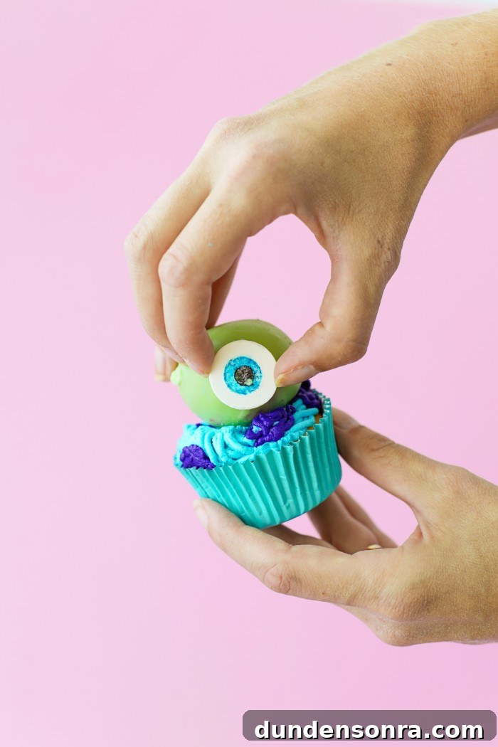 Fondant eye being placed on green cake ball on a cucpake
