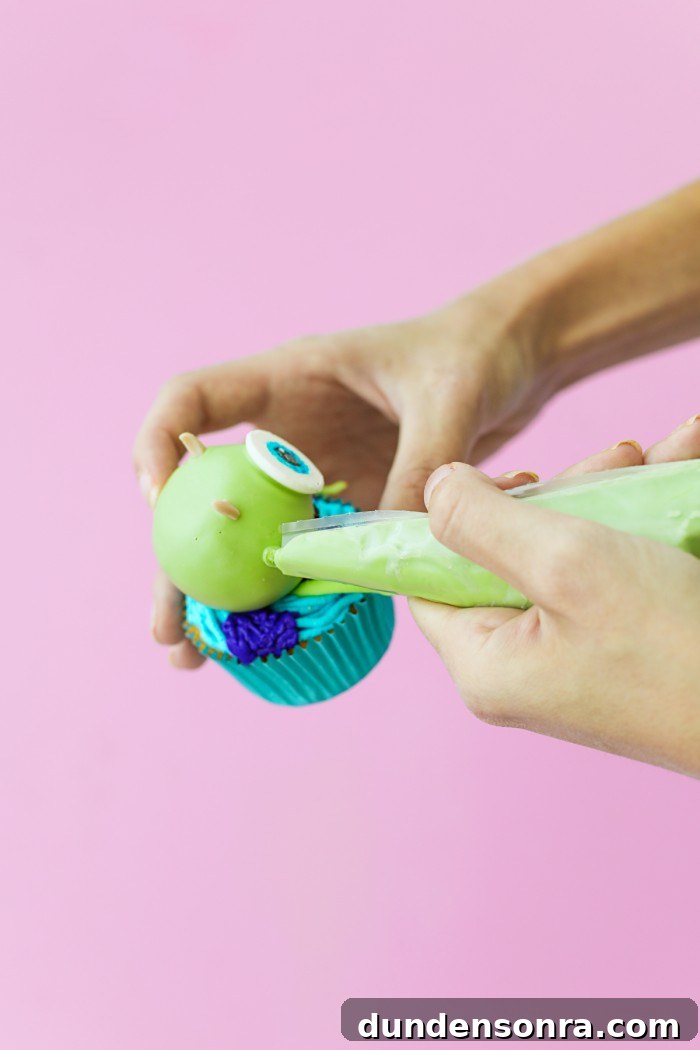 Green Mike Wazowski cake ball onto of a cupcake with icing being placed on