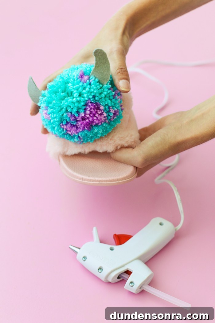 Blue and purple monster Pom Pom being hot glued to a pink slipper