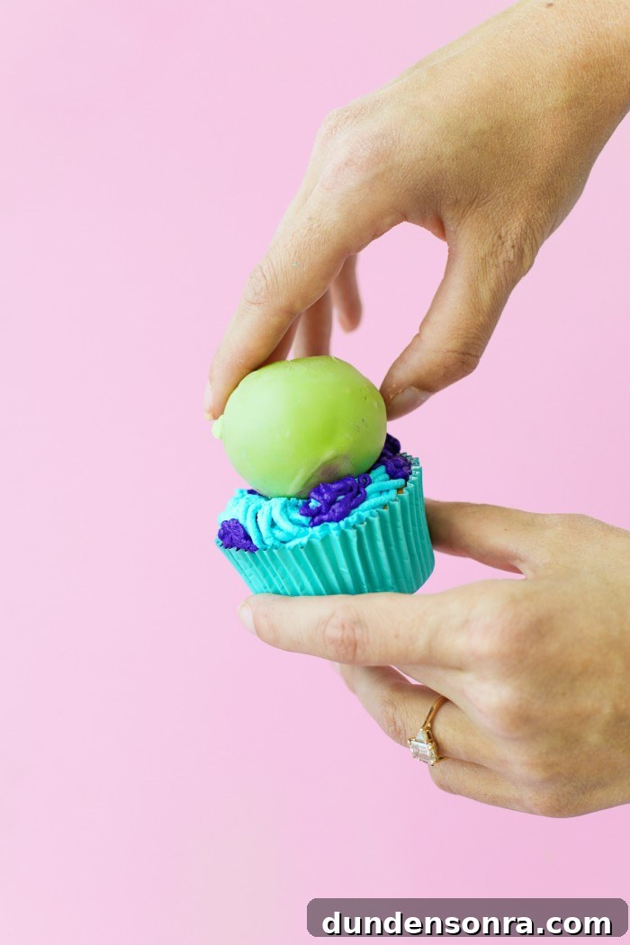 Green cake ball onto of blue and purple frosted Monster cupcake