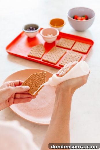 Someone putting frosting on a house shaped graham cracker