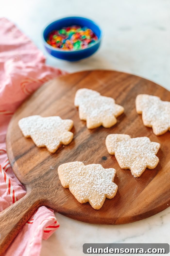 Sugar cookies in the shape of trees on a wooden cutting board. 