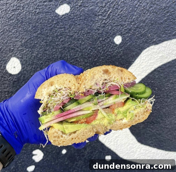 Top Sandwich Spots in Los Angeles: Where Locals Go 10 Vegetarian bagel sandwich held by hand in a blue glove