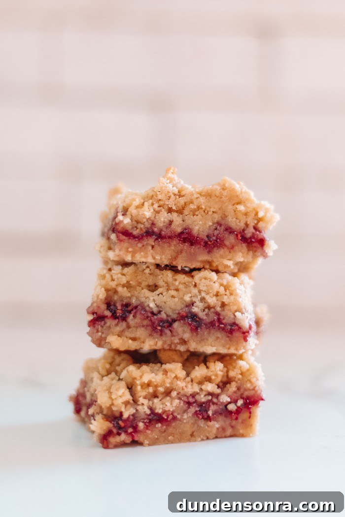 Three raspberry bars stacked in front of white tile