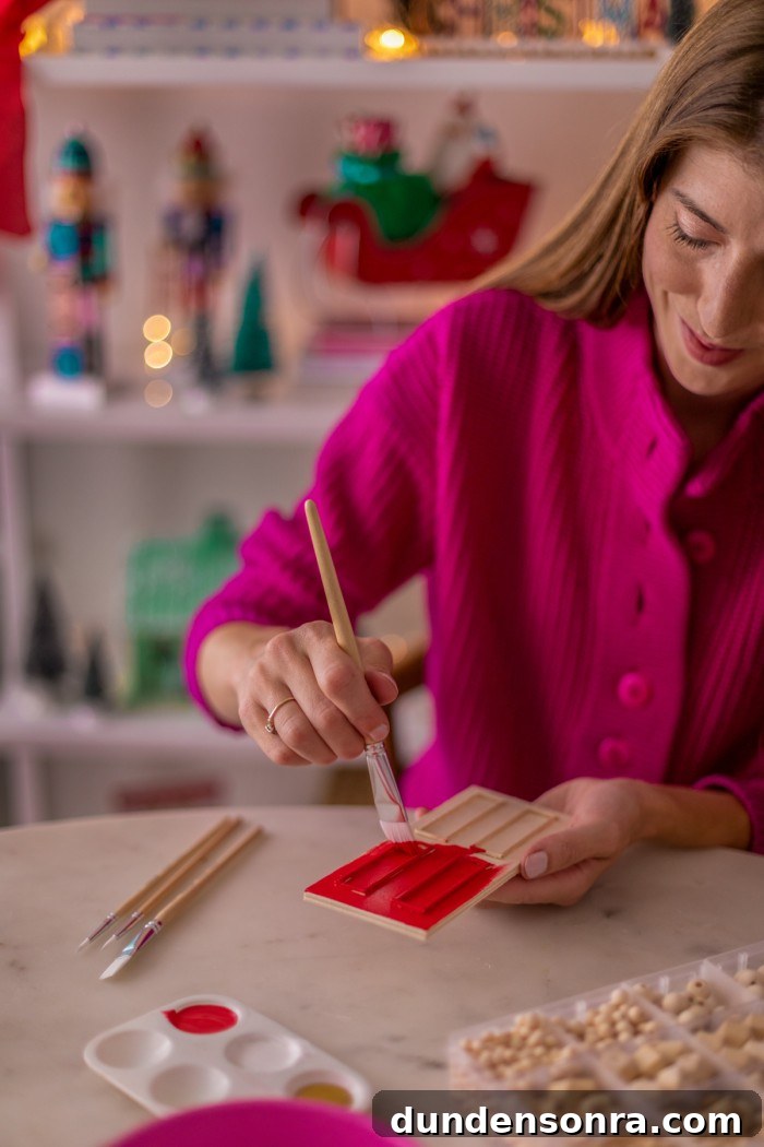 Woman holding a paint brush and painting a mini door red. 
