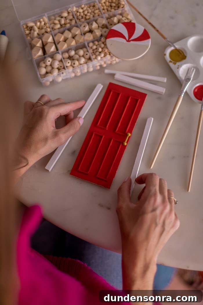 Hands holding two wooden dowels to create a frame around the small red door. 