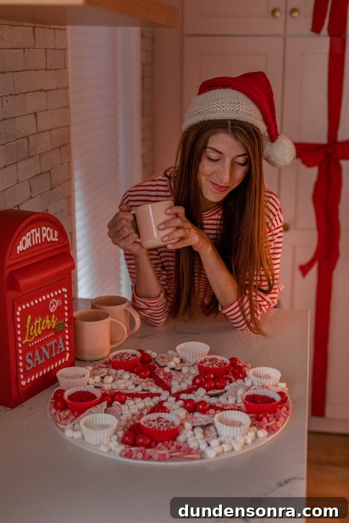 Hot Chocolate Toppings Christmas hot chocolate board with a woman in the background holding a mug and wearing a Santa hat.