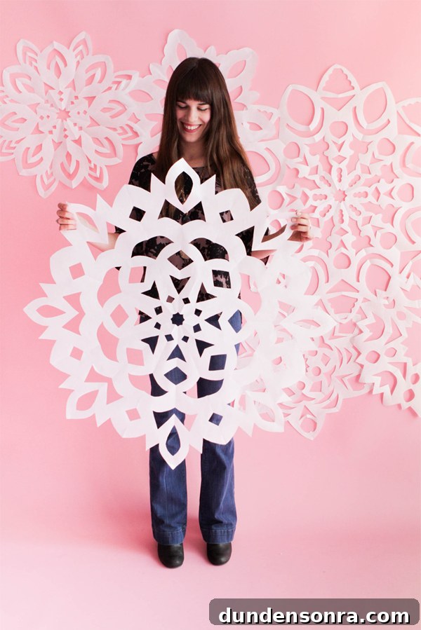 Snowflake Christmas Costume Woman holding a large paper snowflake with more snowflakes on the pink wall behind her.