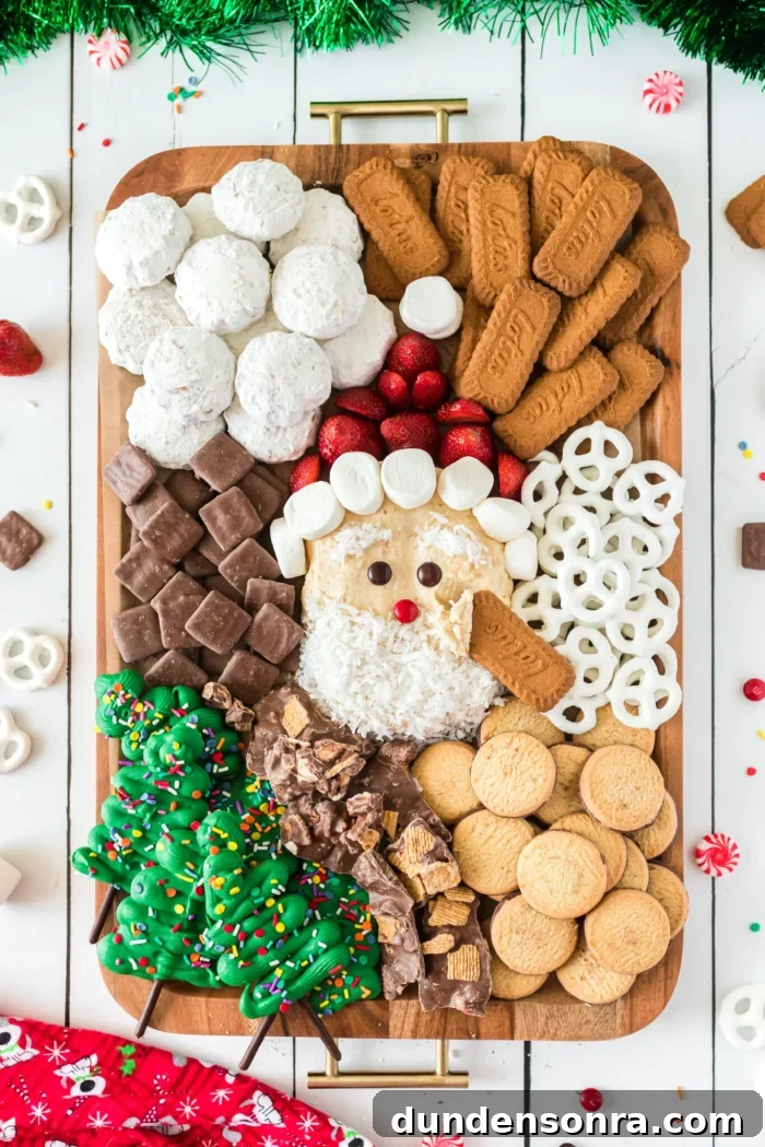Santa Charcuterie Dessert Board Santa cheesecake ball surrounded by cookies and pretzels on a wooden board.