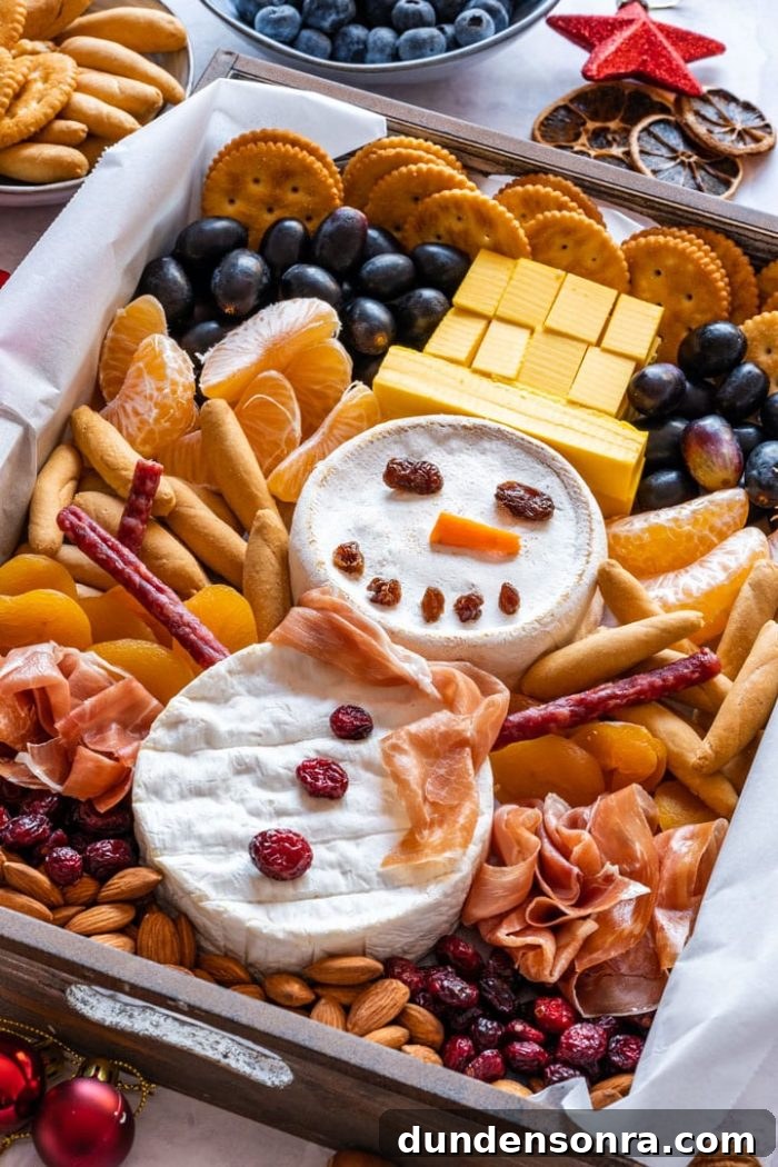 Snowman Charcuterie Board Snowman made of brie surrounded by crackers, meats and fruit.