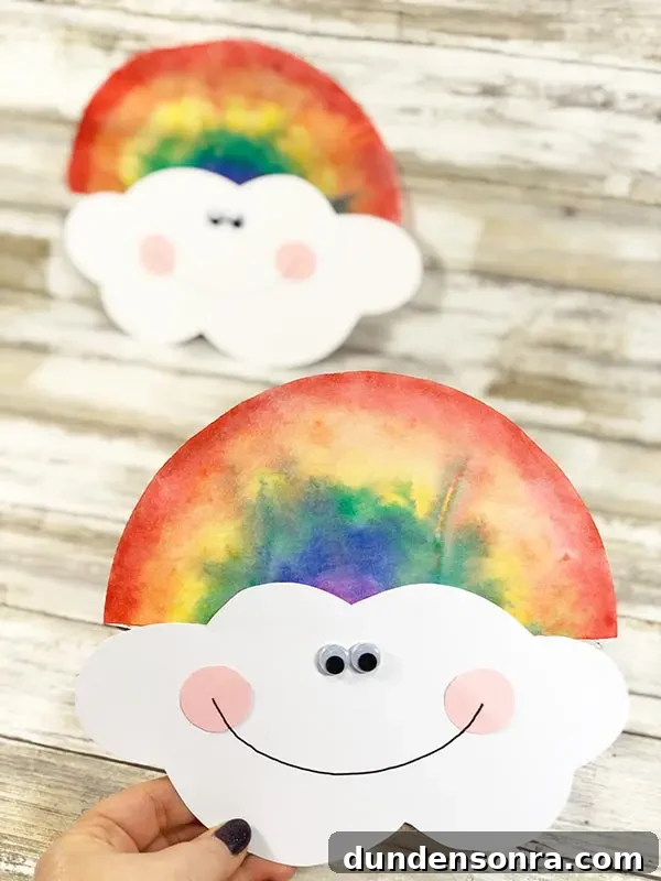 Rainbow Coffee Filter Craft Hand holding a paper cloud with a coffee filter rainbow on top of it.