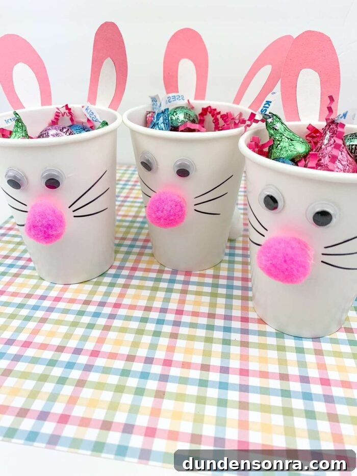 Three white paper cups with bunny faces on them and filled with candy. 