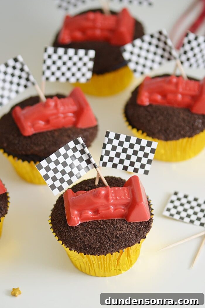 Cupcakes topped with crushed cookies and a race car with flags. 