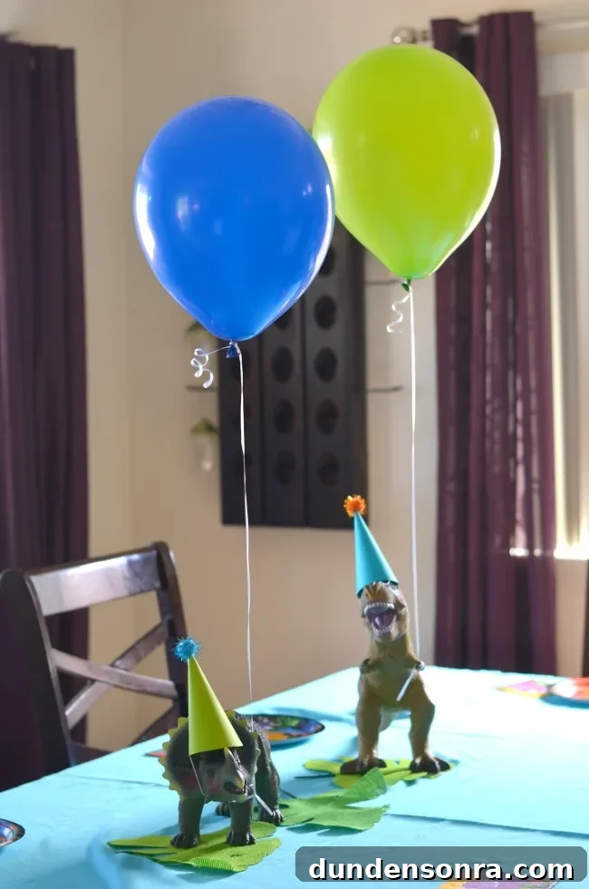 Two dinosaur figures on a table with party hats and balloons. 