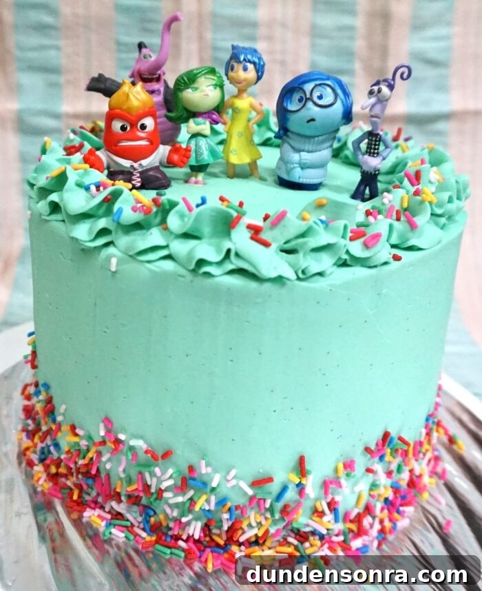 Blue cake with rainbow sprinkles and Inside Out character figures on top. 